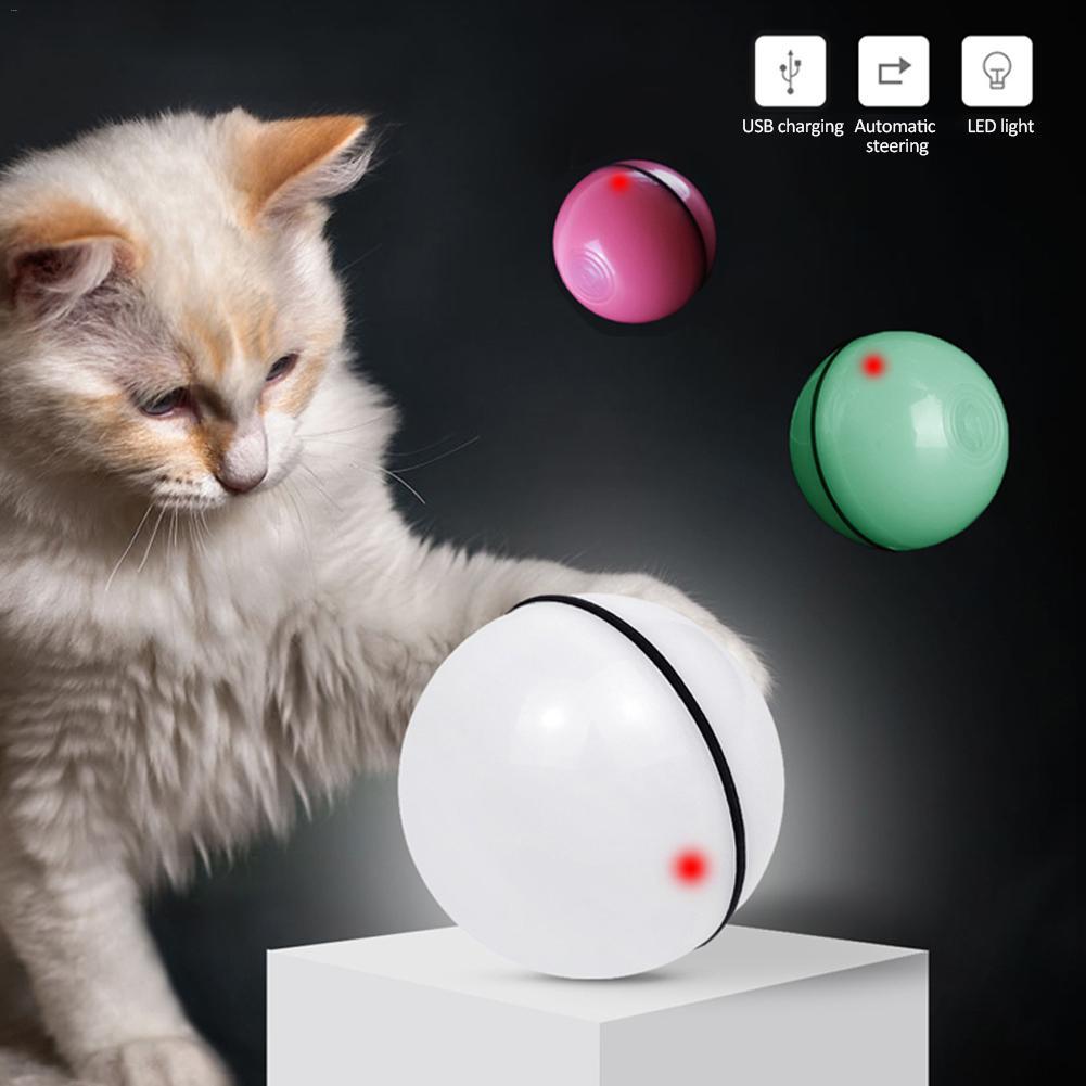 A fluffy white cat is playing with a round electronic rolling ball toy that lights up with LED colors. Multiple colorful rolling balls appear around it, showing features like USB charging and automatic steering.